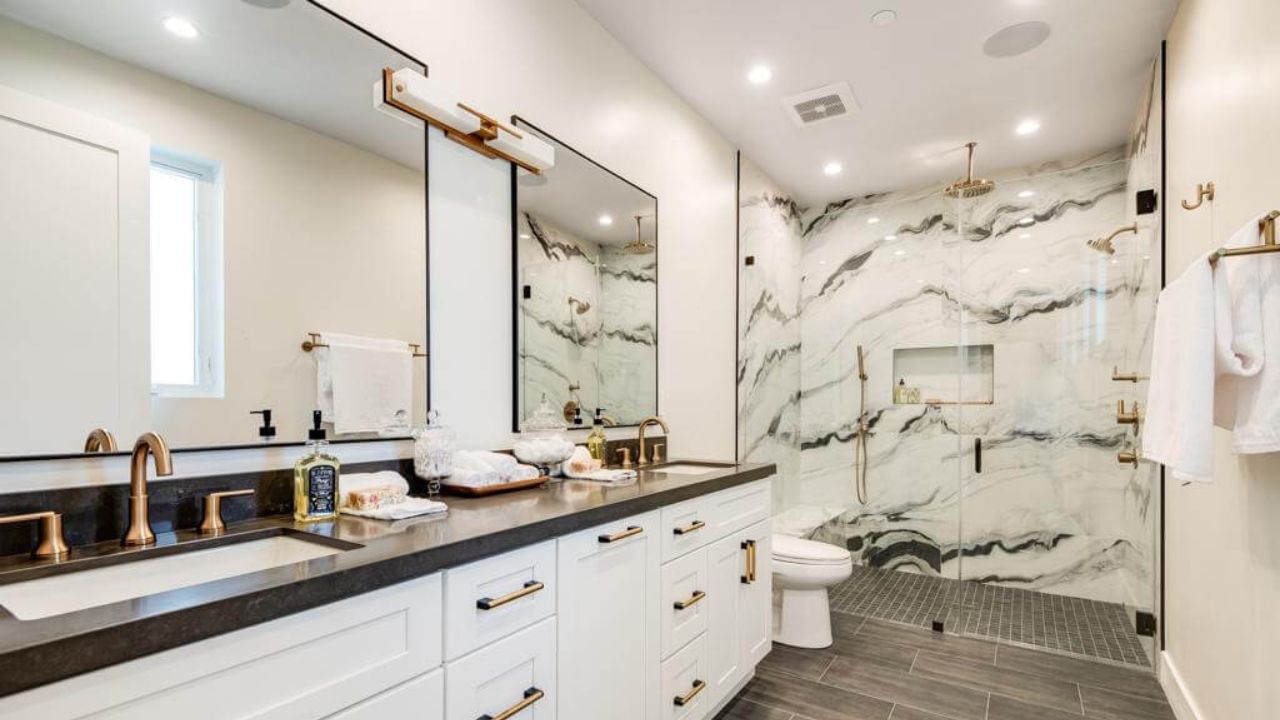 Modern luxury bathroom featuring a spacious walk-in shower with striking black and white marble walls, dual vanity sinks with dark countertops, white cabinetry, and brushed gold fixtures—an elegant example of high-end bathroom remodeling services.