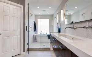 This modern bathroom features a luxurious freestanding tub and a sleek, glass-enclosed shower. The vanity boasts a minimalist design with a large, white countertop and contemporary dark wood cabinetry. Stylish lighting and polished fixtures add to the sophisticated atmosphere, while the light-colored tiles and neutral tones create a serene space. For transforming your bathroom into a tranquil retreat, choose a Professional Remodeling Company to ensure expert craftsmanship and elegant design.