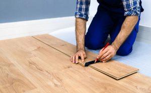 Worker measuring and marking wooden planks during installation, representing professional flooring services for precise and high-quality results.