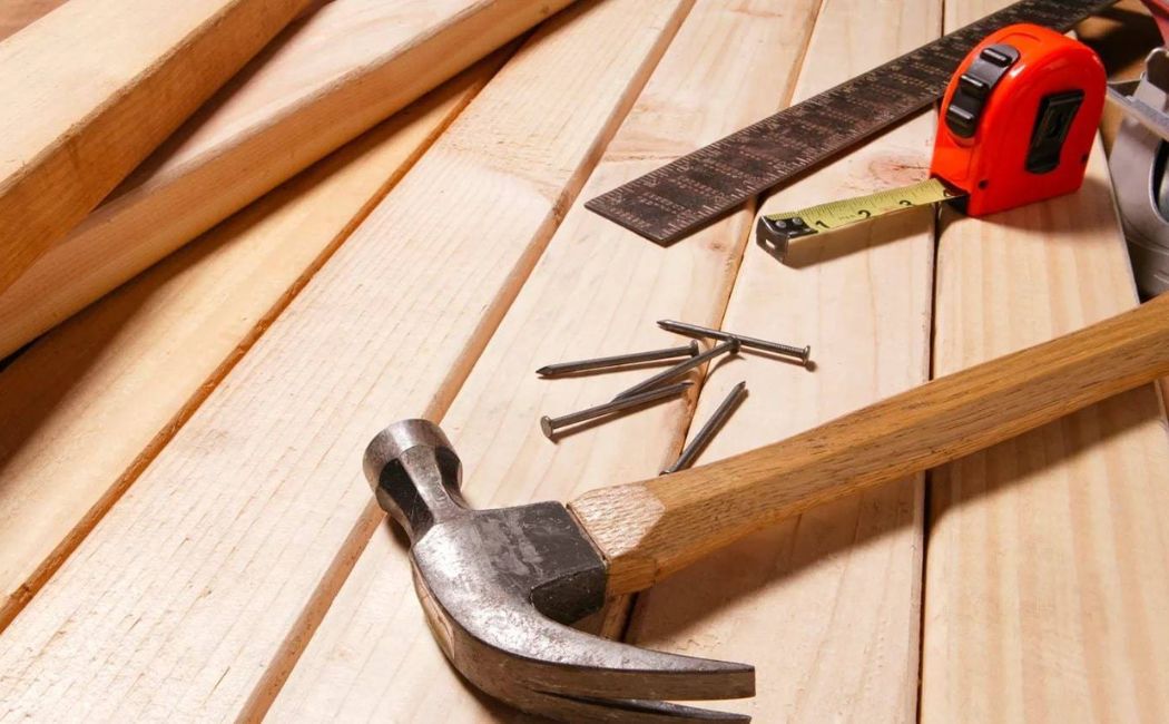 Professional carpentry services with wooden planks, hammer, nails, measuring tape, and carpenter tools neatly arranged on a workbench.