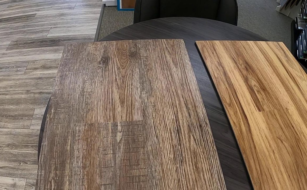 The image showcases two laminate flooring samples placed on a table, offering different wood finishes, displayed by a laminate flooring company.