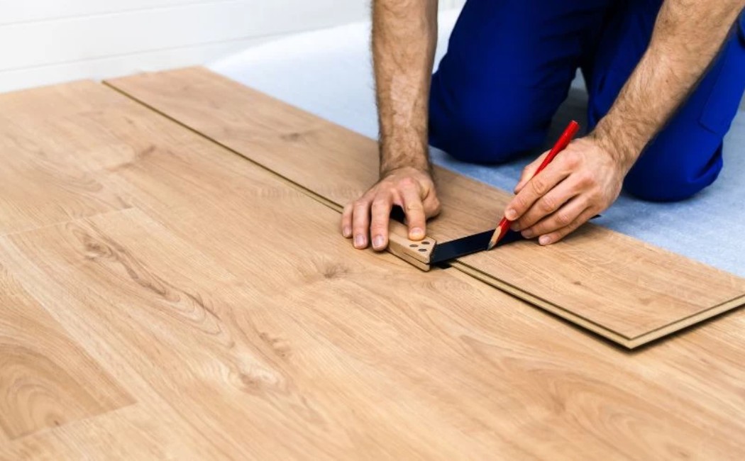A professional installing laminate flooring, carefully measuring and marking the planks for a perfect fit. Expert laminate flooring services for a flawless finish.