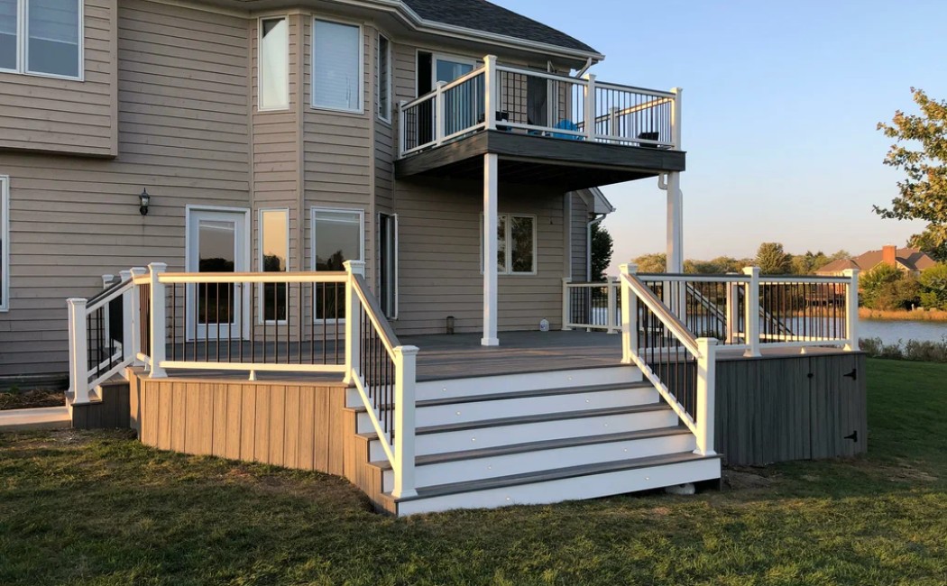 Custom Multi-Level Deck by Professional Deck Building Company Multi-level backyard deck attached to a modern home, featuring wide stairs, white railings, and an upper balcony. Professional outdoor living space designed by a trusted Deck Building Company.