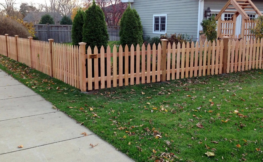 Professional Fence Repairing Services for Durable and Attractive Picket Fences A neatly installed wooden picket fence along a residential lawn and sidewalk, showcasing professional Fence Repairing services that improve durability, safety, and curb appeal.