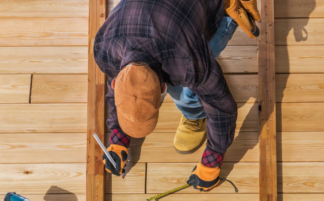 Worker measuring and installing wooden deck boards with tools, demonstrating Professional Deck Maintenance Services for durable and precise outdoor construction.