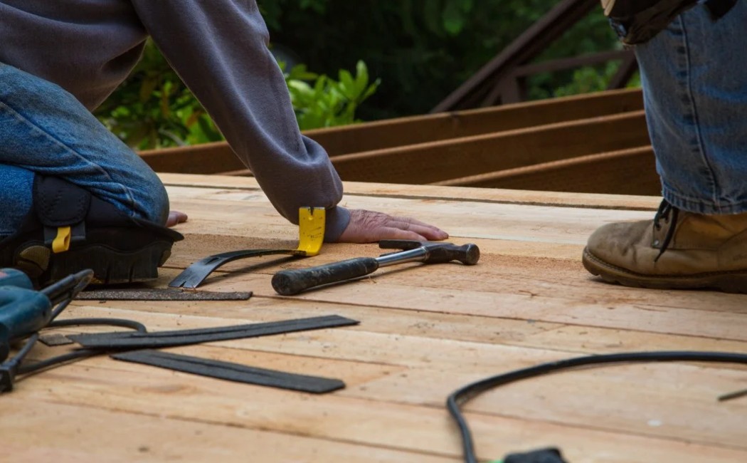 Workers repairing wooden boards with tools during professional Deck Maintenance Services on an outdoor deck.