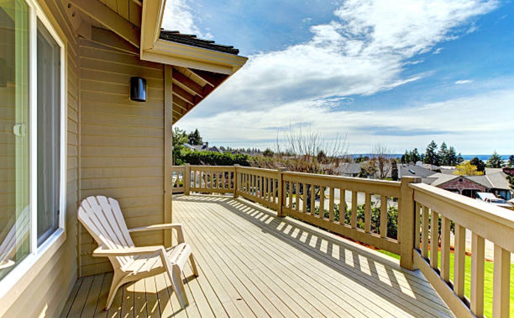Spacious wooden balcony overlooking a scenic neighbourhood and water view, showcasing clean railings and well-kept flooring ideal for Deck Maintenance Services.