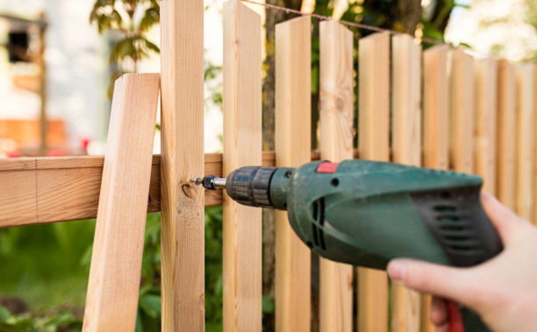 Close-up of a worker using a power drill to secure wooden fence panels, highlighting professional Fence Maintenance Services for strong and durable fencing.