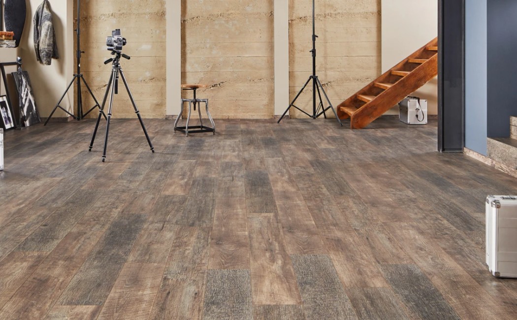 Spacious studio-style living area with rustic wood-look floors, leather seating, and modern décor, beautifully installed by a professional Laminate Flooring Company.