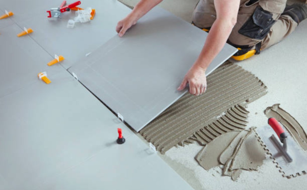 A professional tile installer carefully placing large floor tiles over adhesive mortar using leveling clips during a home flooring installation.