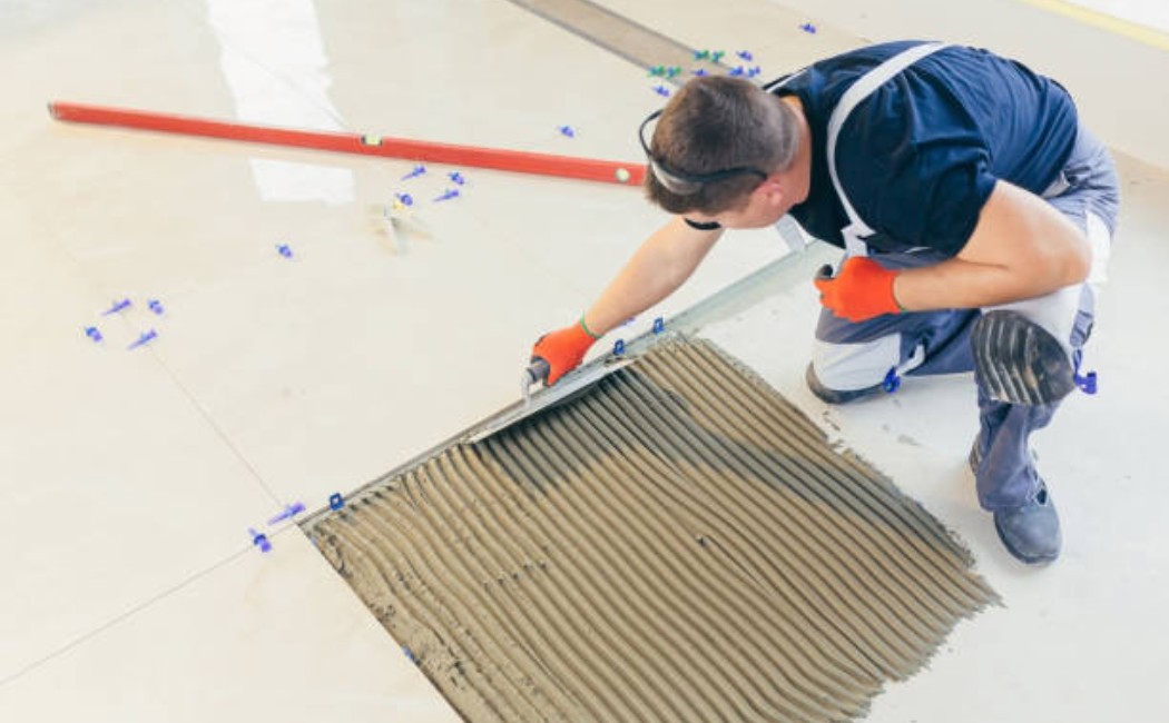 Worker applying adhesive with a notched trowel during Tile Installation Services, preparing the floor for large ceramic tiles.