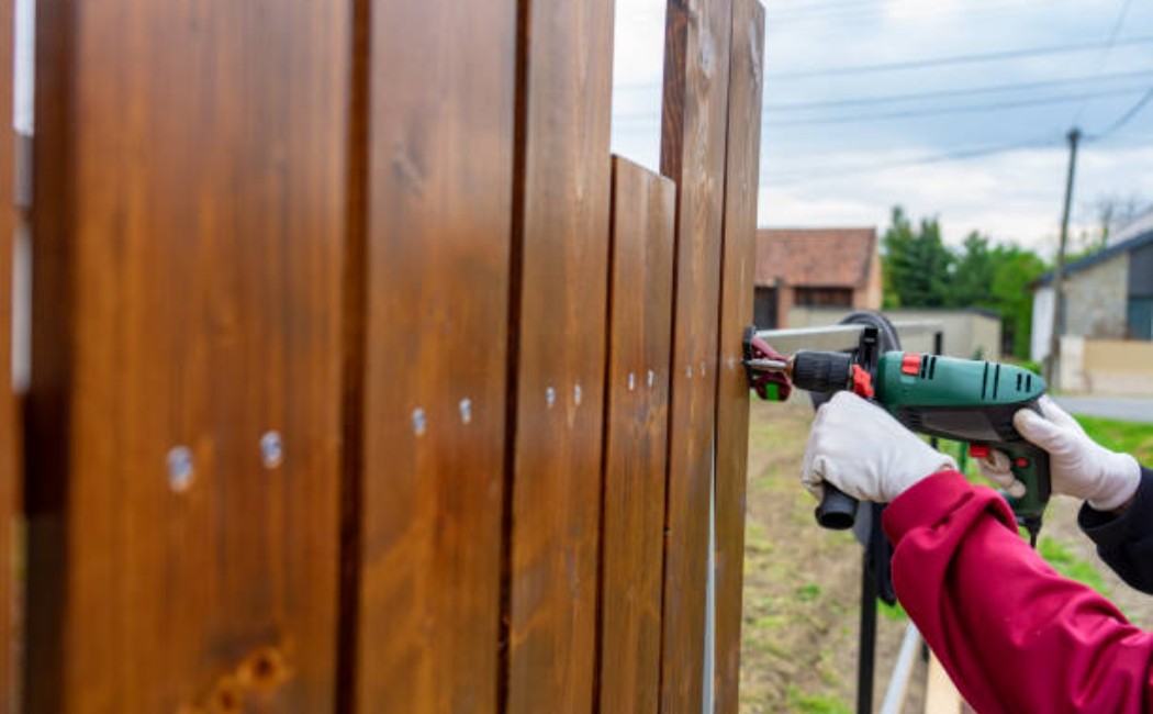 Worker using a power drill to secure wooden panels during a professional Fence Installation project outdoors.