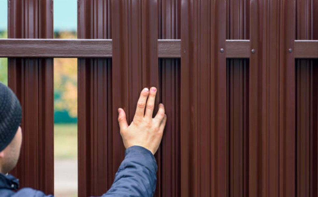 Person touching a newly installed metal fence during a Fence Build process outdoors.