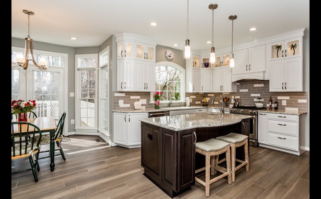 Bright, modern kitchen with white cabinetry, a dark wood island, pendant lighting, and large windows—an example of work by a professional Kitchen Remodeling Company.