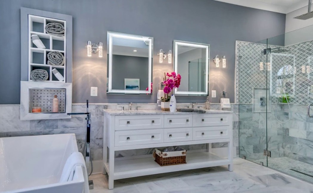 Modern luxury bathroom featuring a double vanity with illuminated mirrors, marble tiles, a glass walk-in shower, and a freestanding tub, showcasing elegant Bathroom Remodeling design and organization.