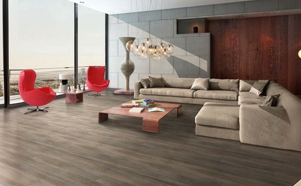 Modern Living Room by a Laminate Flooring Company Modern living room with wide plank wood-look floors, large windows, sectional sofa, and stylish red chairs, showcasing expert craftsmanship by a Laminate Flooring Company.